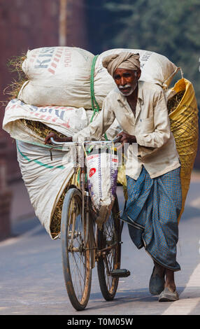 AGRA, INDIA - NOVEMBER 16, 2012: Indian man rolls his bike with a big bag Stock Photo