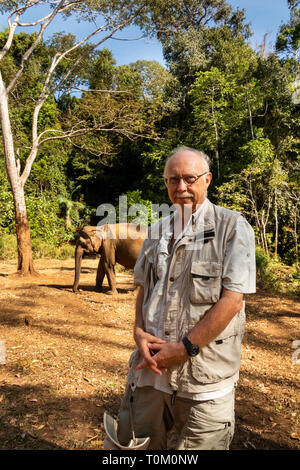 Cambodia, Mondulkiri Province, Sen Monorom, Elephant Valley Project, senior male visitor close to former working elephant in forest clearing Stock Photo