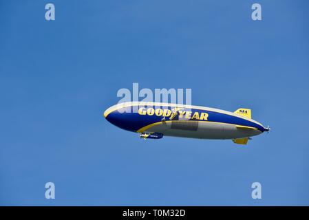 Famous Goodyear blimp dirigible soaring overhead in flight in bright blue sky, outside sporting event, PGA golf tournament, San Diego, CA, USA. Stock Photo