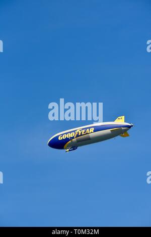 Famous Goodyear blimp dirigible soaring overhead in flight in bright blue sky, outside sporting event, PGA golf tournament, San Diego, CA, USA. Stock Photo