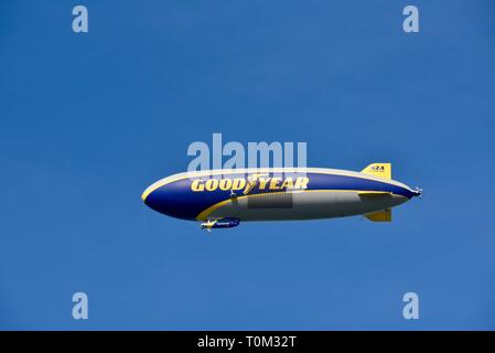 Famous Goodyear blimp dirigible soaring overhead in flight in bright blue sky, outside sporting event, PGA golf tournament, San Diego, CA, USA. Stock Photo