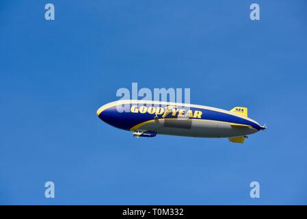 Famous Goodyear blimp dirigible soaring overhead in flight in bright blue sky, outside sporting event, PGA golf tournament, San Diego, CA, USA. Stock Photo