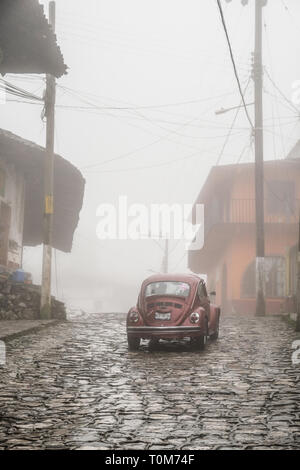 An old Volkswagen Beetle car moving on cobblestone street in fog at Cuestzalan,Mexico Stock Photo