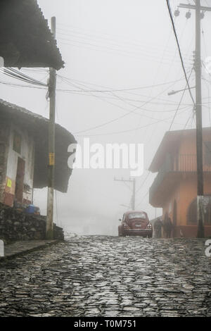 An old Volkswagen Beetle car moving on cobblestone street in fog at Cuestzalan,Mexico Stock Photo