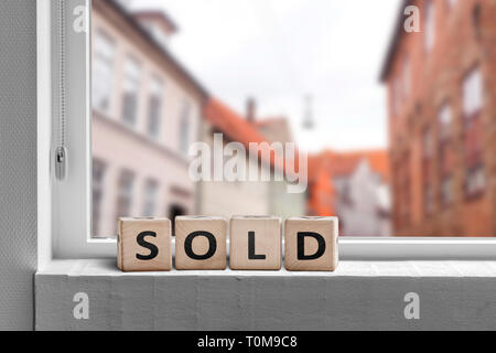 Sold word made with cubes in a window in a city with a view to buildings Stock Photo