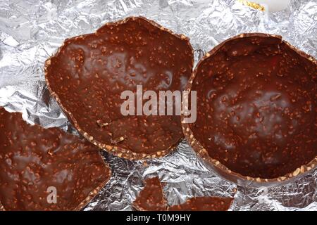 Broken chocolate Easter egg with chopped hazelnuts on a foil sheet against, UK. Stock Photo