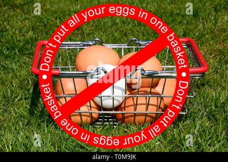 Chicken eggs in a shopping basket on the grass with the wording dont put all your eggs in one basket in a no entry sign, UK. Stock Photo