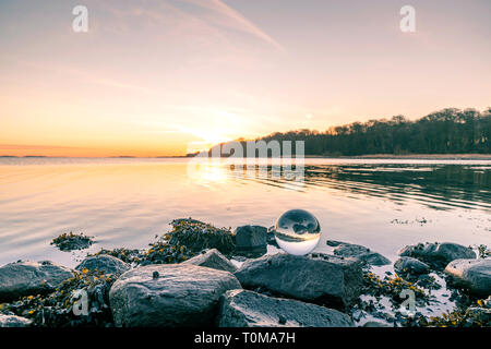 Glass orb on o rock by the lake in a beautiful sunrise an early morning Stock Photo