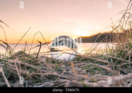 Crystal ball in frozen grass by a lake in the morning sunrise on a cold day Stock Photo