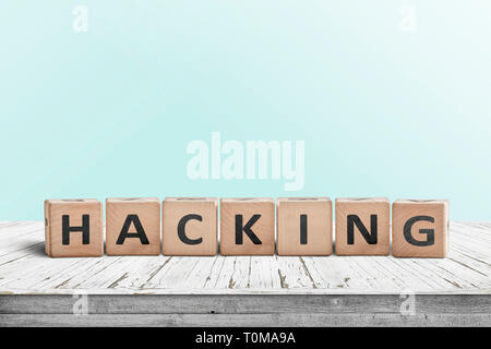 Hacking sign on a wooden table in a bright room with a cyan background Stock Photo