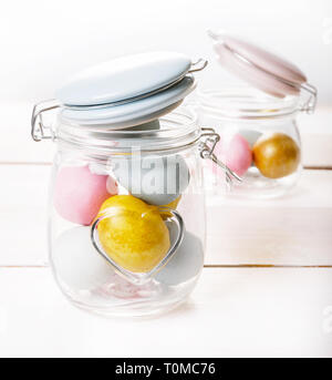 Easter background with pink, blue, golden Easter eggs in glass jar on white wooden desk Stock Photo