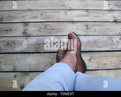 Crossed feet with brown shoes on a wood floor Stock Photo