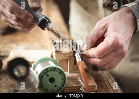 Closeup of hands using a soldering iron on a rustic workbench Stock Photo