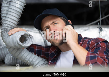 young male technician on the phone repairing air conditioner indoors Stock Photo