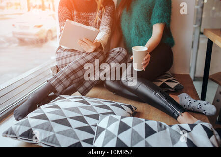 two young woman chatting in a coffee shop. Two friends enjoying coffee together. One girl uses a tablet. Stock Photo