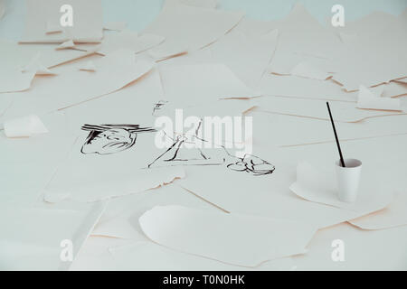 White sheets of paper painted with some black ink illustrations lying on the floor Stock Photo