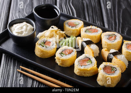 Delicious breakfast Tamagoyaki set sushi roll with rice, omelette, cheese, salmon and avocado close-up with sauces, wasabi and ginger on a plate on th Stock Photo