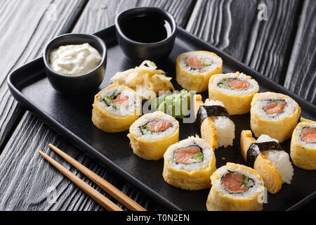 Tamagoyaki set sushi roll with rice, omelette, cheese, salmon and avocado served with sauces, wasabi and ginger on a plate on the table. horizontal