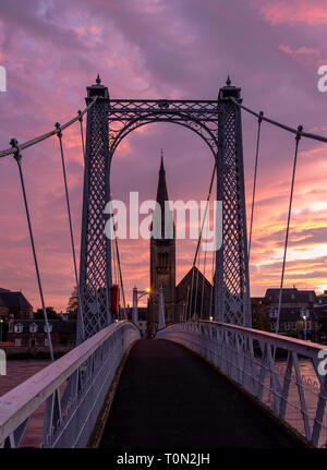 The Greig Street suspension bridge that crosses the River Ness in Inverness; framed around the Free Church of Scotland at dawn. Stock Photo