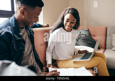 Girl reading book while man making notes on sofa at college campus. Youngsters studying together sitting on a couch at campus building. Stock Photo
