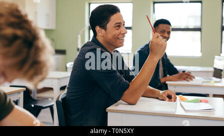 Male student sitting in the class and raising hand up to ask question during lecture. High school student raises hand and asks lecturer a question. Stock Photo