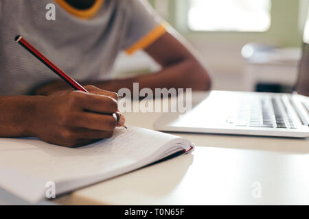 Close up of female student at lecture in classroom. Focus on young woman hands writing notes in a book with laptop on desk. Stock Photo