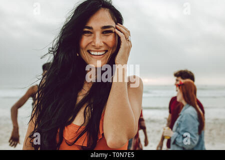 Attractive young woman on the beach smiling. Pretty caucasian female standing at the beach with group of friends in background. Stock Photo