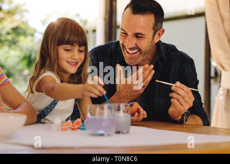 Father and daughter painting easter eggs together. Smiling man helping his daughter paint easter eggs. Stock Photo