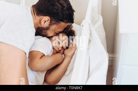 Cheerful father and son having fun at home. Man pampering and waking up his son on bed. Stock Photo