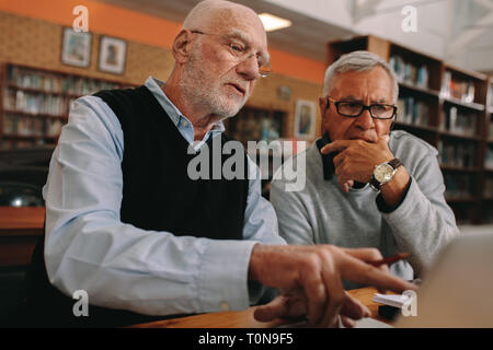 Two elderly gentlemen learning courses on laptop sitting in classroom. Senior men sitting in classroom and discussing their subject on a laptop comput Stock Photo
