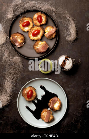 Vertical photo with top view on blue plate with puff pastry cups. Cups are stuffed by melted cheese. Ham and red tomatoes are on baked pastries. Dark  Stock Photo