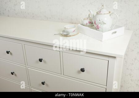 White tea service on white commode ready for use in bedroom on tray. Stock Photo