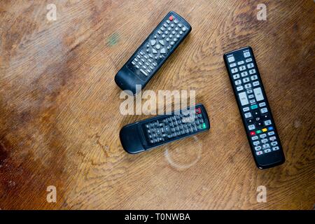 Three old remote controls from televisions and videos on destroyed table surface - concept Stock Photo