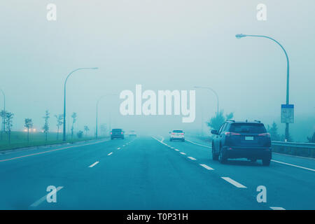 Highway in mystic fog mist smog. Cars on freeway road at evening in american city country. Poor visibility in bad weather conditions. Toned with film  Stock Photo