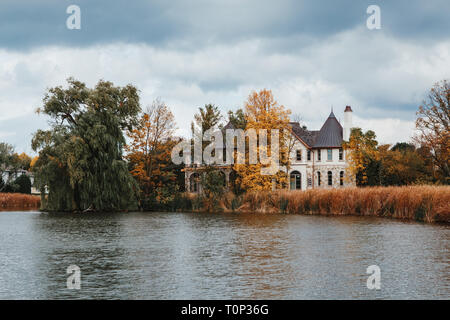 Landscape nature view of beautiful Erupean gothic looking house castle hidden behind trees near pond lake with weeping willow trees and reed grass. Ba Stock Photo