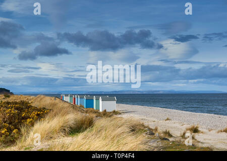 FINDHORN BEACH MORAY FIRTH SCOTLAND COLOURED CHALETS OR BEACH HUTS ON PEBBLE BEACH SNOW OVER THE HILLS AND BLACK ISLE