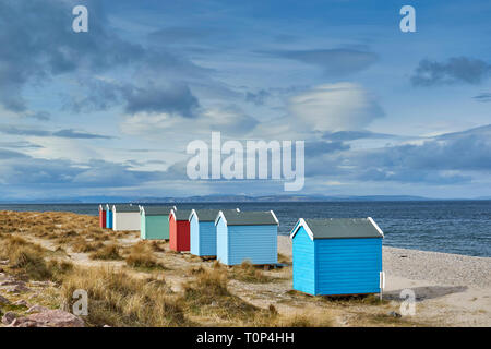 FINDHORN BEACH MORAY FIRTH SCOTLAND EIGHT PASTEL COLOURED CHALETS OR BEACH HUTS ON PEBBLE BEACH SNOW OVER THE HILLS AND BLACK ISLE