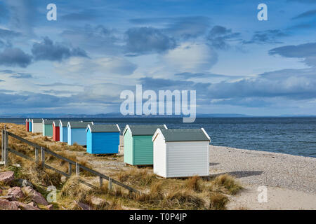 FINDHORN BEACH MORAY FIRTH SCOTLAND PASTEL COLOURED CHALETS OR BEACH HUTS ON PEBBLE BEACH SNOW OVER THE HILLS AND BLACK ISLE