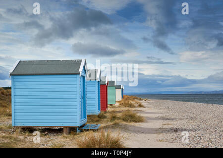 FINDHORN BEACH MORAY FIRTH SCOTLAND PASTEL COLOURED CHALETS OR BEACH HUTS ON PEBBLE BEACH WITH SEA GRASS SNOW OVER THE HILLS AND BLACK ISLE