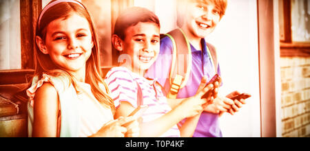 Portrait of school kids using mobile phone in corridor Stock Photo