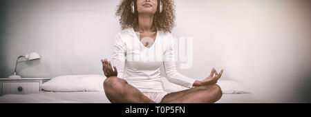 Woman listening to music on head phones while meditating on bed Stock Photo