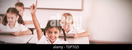 Smiling schoolgirl raising hand in classroom Stock Photo