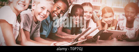 Teacher and kids lying on floor using digital tablet in library Stock Photo