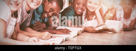 Teacher and kids lying on floor reading book in library Stock Photo