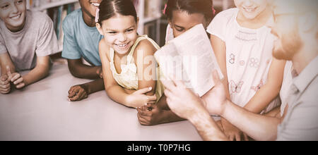 Teacher with book teaching students in library Stock Photo