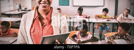 Teacher posing in front of class with tablet pc Stock Photo