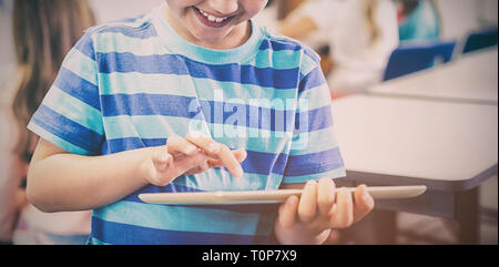 Smiling schoolboy using digital tablet in classroom Stock Photo