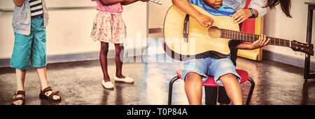 Teacher assisting a kids to play a musical instrument in classroom