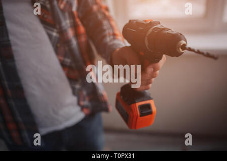 The worker or builder holds an electric drill. Building or repair concept. Against the background of construction. Stock Photo