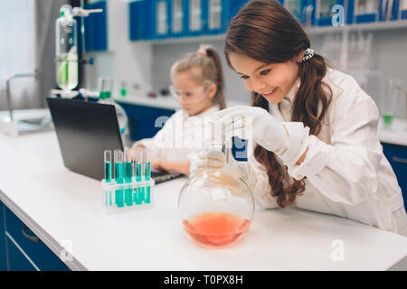 Two little kids in lab coat learning chemistry in school laboratory. Young scientists in protective glasses making experiment in lab or chemical cabin Stock Photo